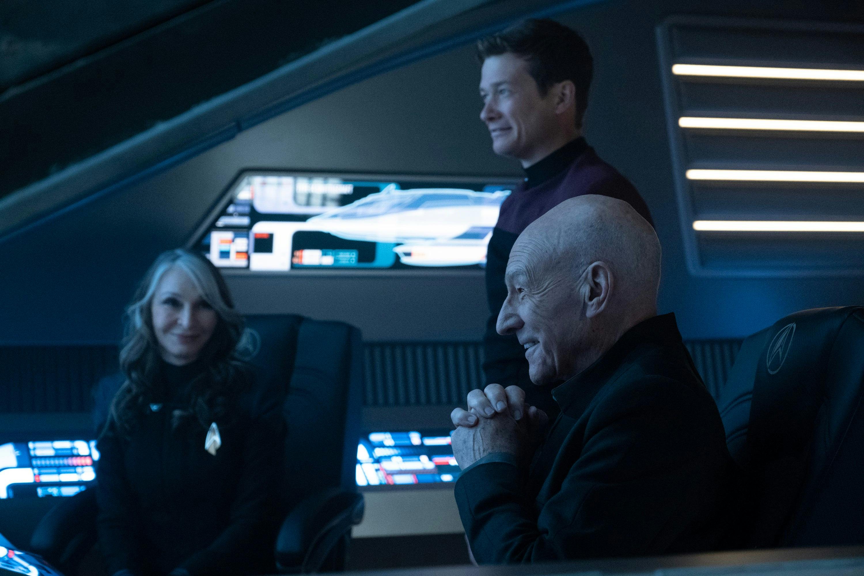On a shuttle, Jean-Luc and Jack Crusher look forward smiling as Beverly Crusher smiles facing Jean-Luc in 'The Last Generation'